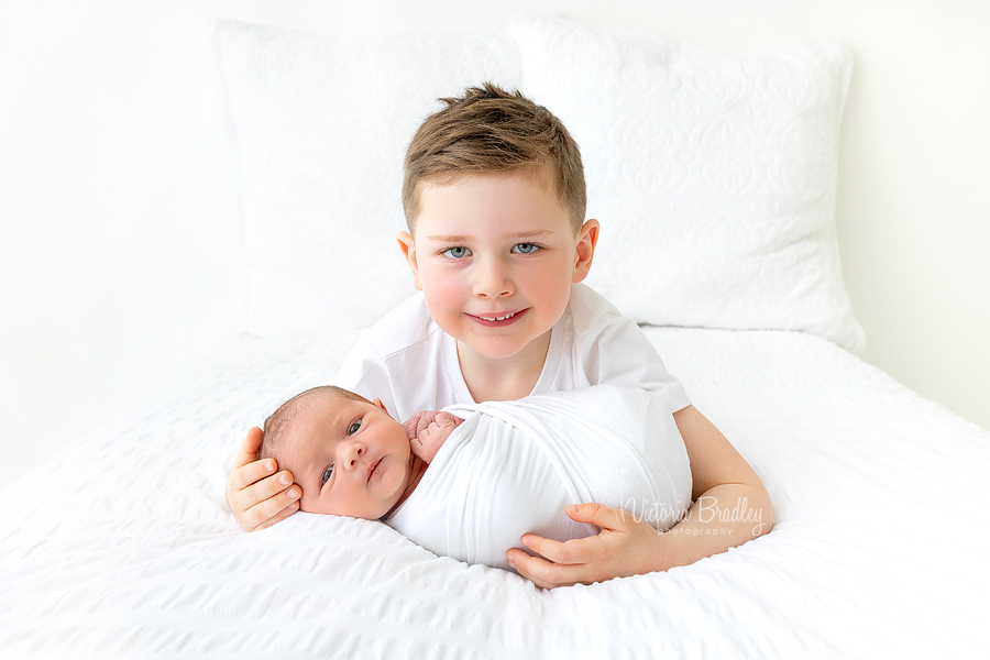 sibling and newborn on white
