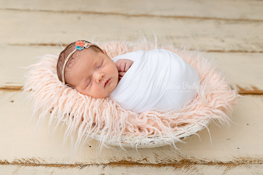 swaddled newborn in white on pink fur in white bowl
