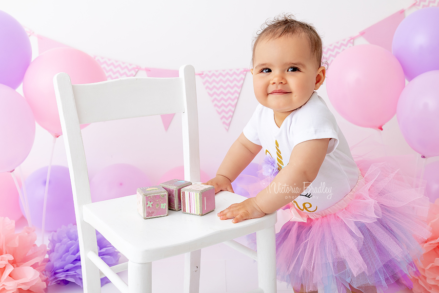 smiling baby girl in pink and purple cake smash photography with balloons