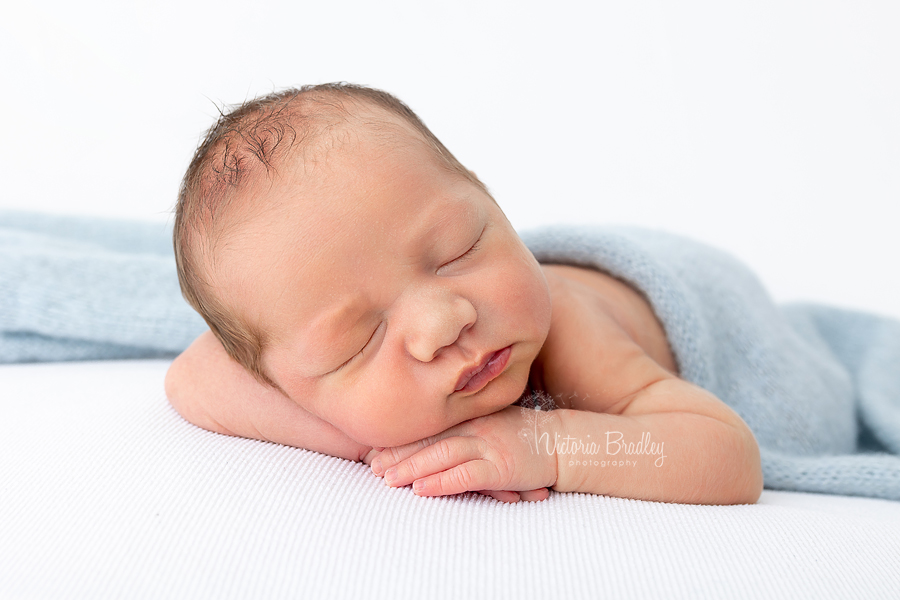 Newborn baby boy on white backdrop with blue wrap