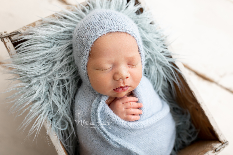 swaddled newborn in duck egg blue wrap in wooden crate