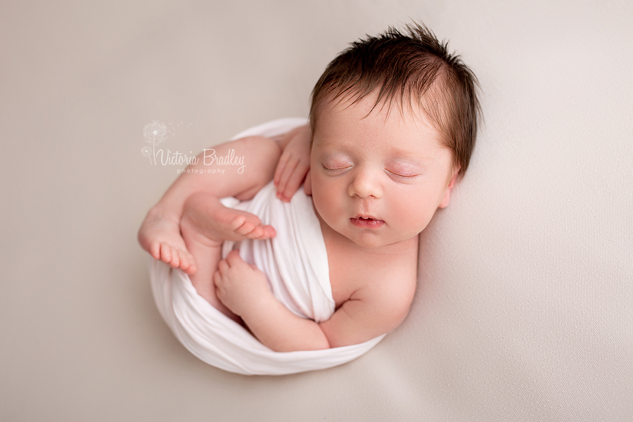 asleep newborn baby on taupe backdrop in white wrap