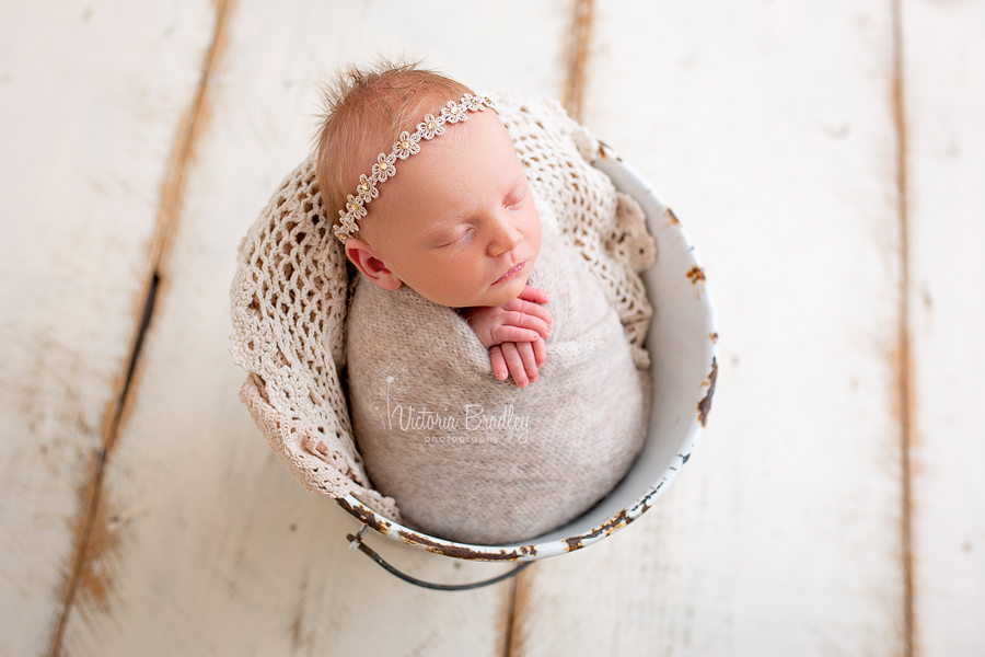 swaddled newborn in white metal bucket with flower tie back