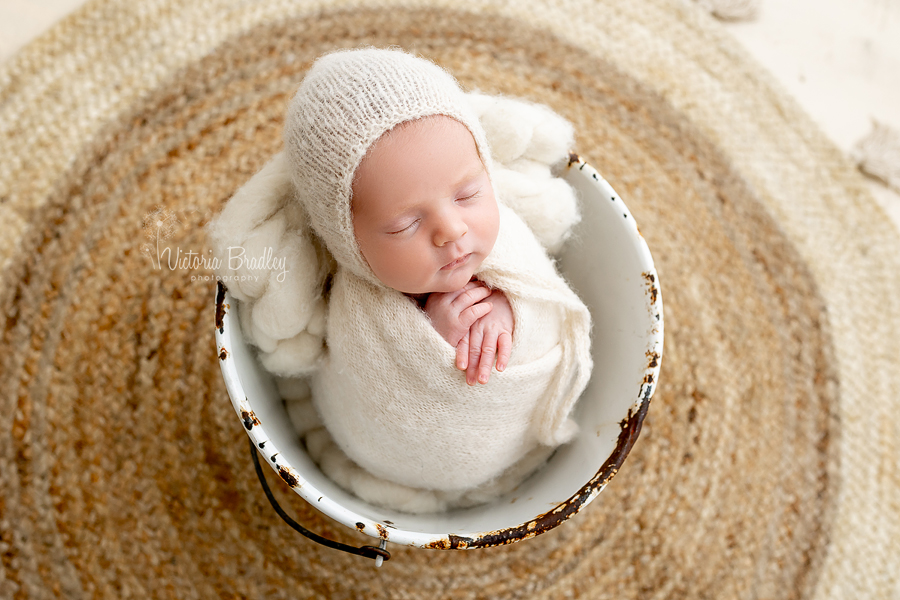 newborn in bucket on jute rug
