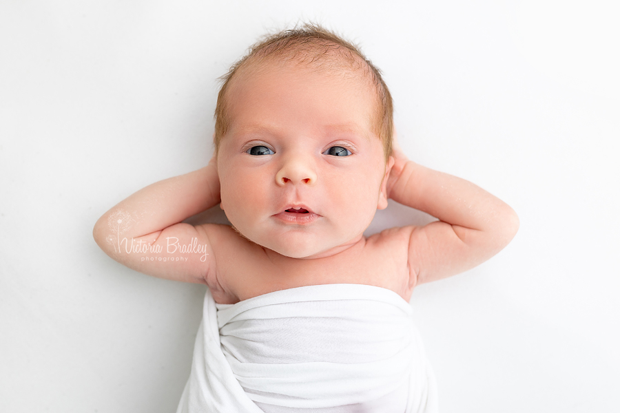 awake newborn baby with hands behind head