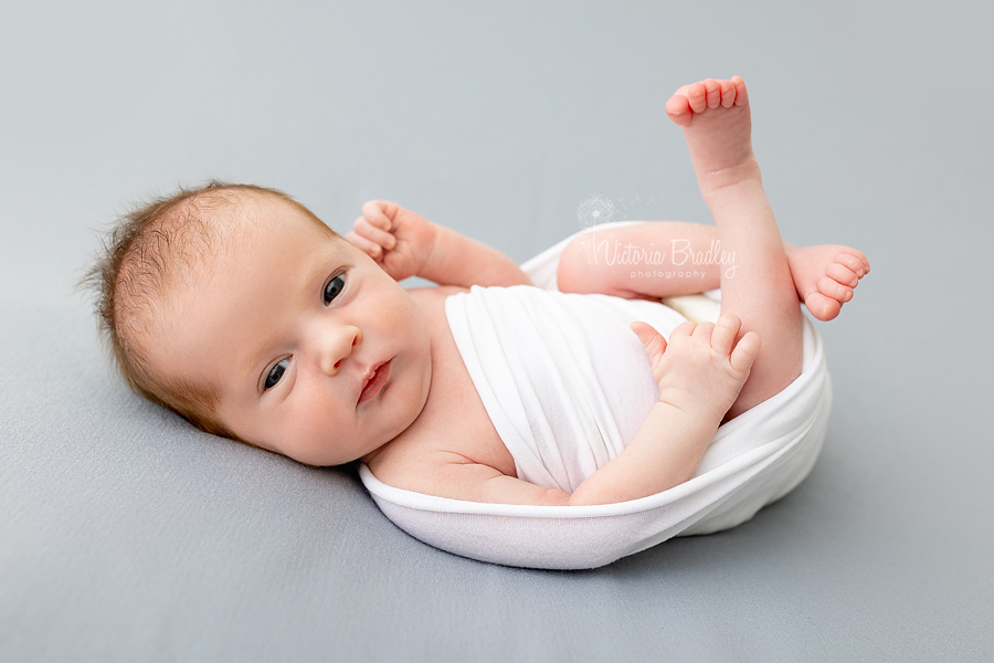 awake newborn on grey backdrop in white wrap