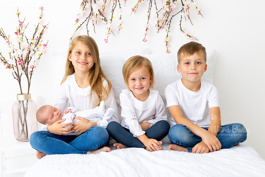newborn with siblings white backdrop with flowers