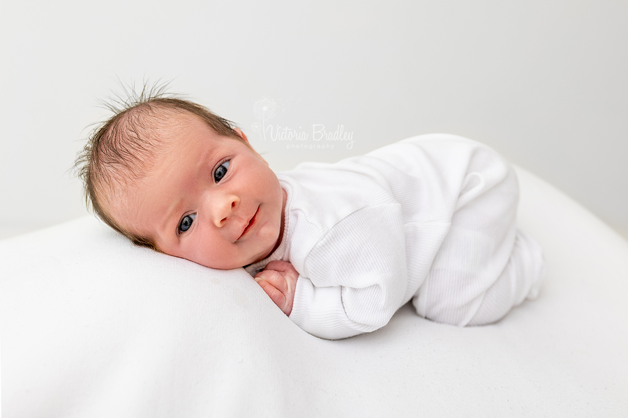 Awake newborn on tummy on white backdrop