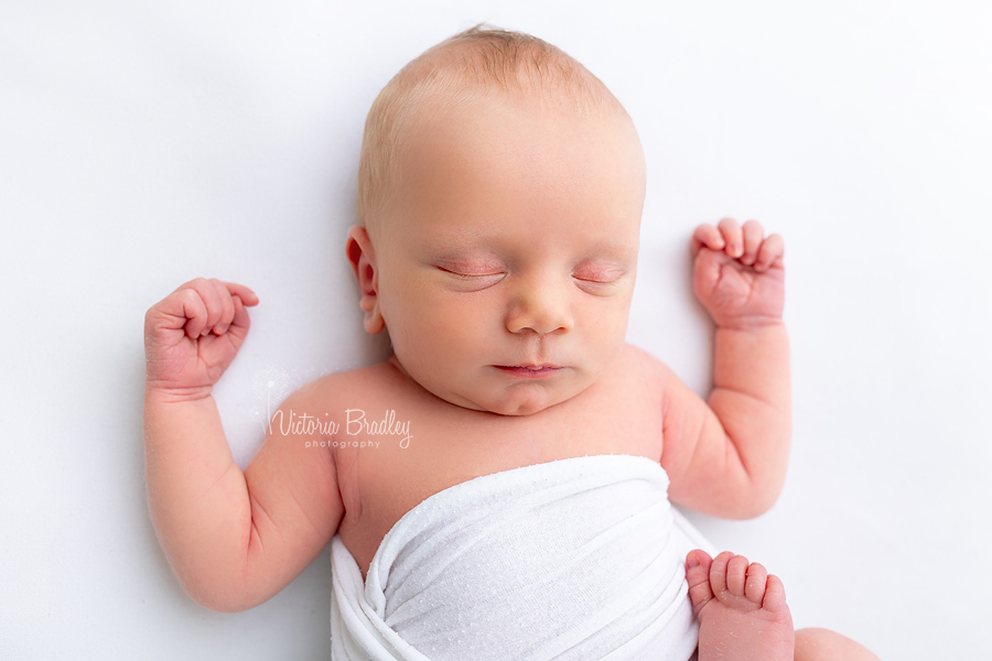sleepy newborn on white backdrop with hands up