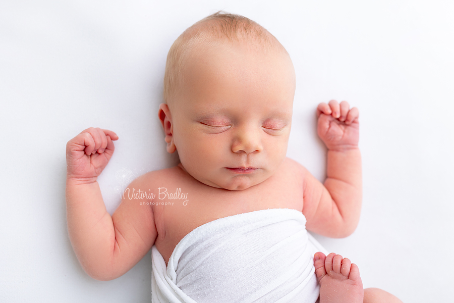 sleepy newborn on white backdrop with hands up