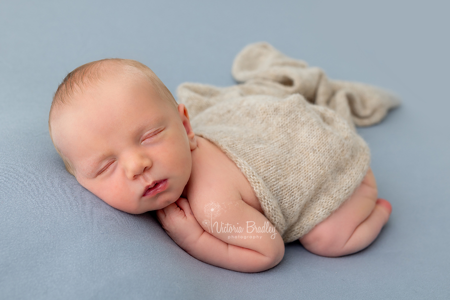 sleepy newborn on tummy on grey backdrop