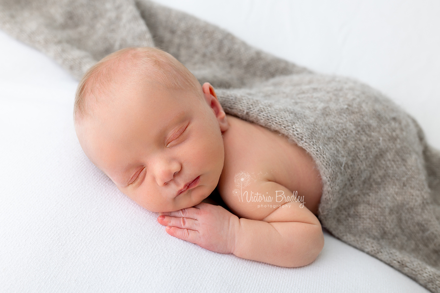 sleepy newborn on tummy with grey knitted wrap