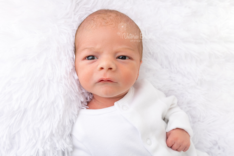 awake newborn on fluffy white rug 